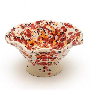 May include: A ceramic bowl with a pedestal base, featuring a speckled pattern of red, black, and orange dots on a cream-colored background. The bowl has a wavy rim.