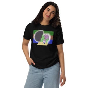 Puede incluir: Camiseta negra con un gráfico de una persona de piel verde besando un cerebro rosa. La persona tiene un afro y está sobre un fondo de rayas azules, verdes y marrones. La camiseta tiene un cuello amarillo.
