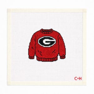 May include: A red sweater with a black and white "G" logo, likely representing a college or university. The sweater is on a white background with the letters "C+H" in the bottom right corner.