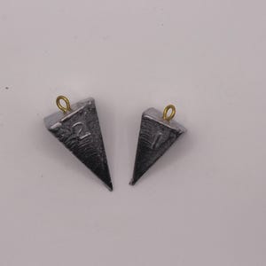 May include: Two gray, triangular fishing weights with a gold-colored loop at the top. One weight is marked with the number "2", and the other with the number "1". The weights are set against a white background.