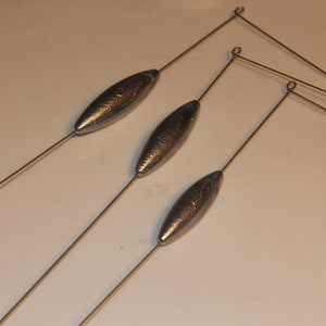 Puede incluir: Tres plomos de pesca plateados con lazos de alambre unidos. Los plomos son de forma ovalada y tienen una superficie texturizada.