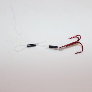 May include: A close-up of a fishing rig with two black beads and a red treble hook.