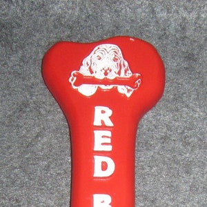May include: Red bone shaped dog chew toy with a white dog illustration and the words "RED BONE" printed on the front.