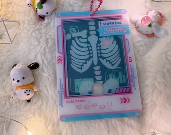 May include: A pink and blue plastic keychain with a cartoon x-ray image of a skeleton. The keychain has the text "WARNING! HYDRATION DETECTED" and "ANALYZING..." on it.