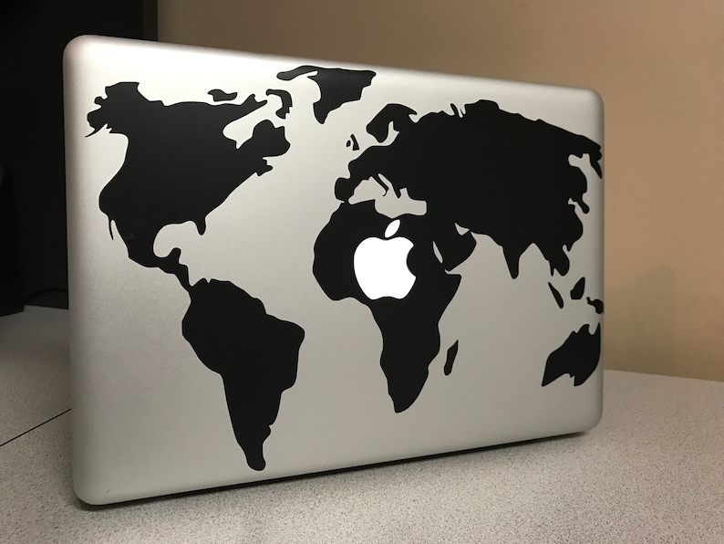 May include: A silver laptop with a black world map design. The Apple logo is visible in the center of the map. The laptop is on a light gray surface.
