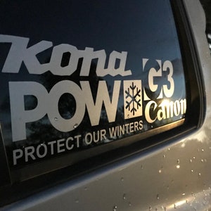 May include: White sticker on a car window with the words "Kona POW" in large, stylized letters. Below, it reads "PROTECT OUR WINTERS". A snowflake graphic is included. The sticker is on a car.