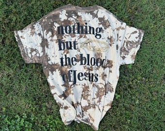 May include: A short-sleeved t-shirt with a brown and white tie-dye pattern. The shirt features black text that reads nothing but the blood of Jesus, with a small, light-coloured graphic of a crown of thorns positioned above the word blood.