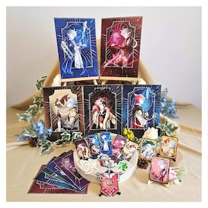 Puede incluir: Colección de impresiones y tarjetas de arte de fantasía. Las impresiones, en tonos azules y rojos, se exhiben en pequeños caballetes de madera. Varias tarjetas y pegatinas están dispuestas alrededor de una base de madera. La obra representa personajes.