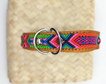 May include: A colourful dog collar with a geometric pattern in shades of pink, green, blue and black. The collar is made of leather and has a silver metal buckle.