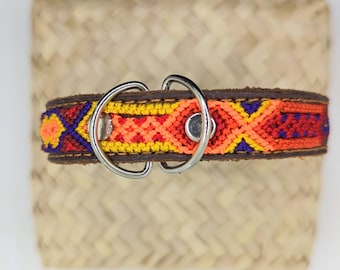 May include: A colourful dog collar with a woven orange, yellow, red and blue pattern. The collar is made of leather and has a silver metal buckle.