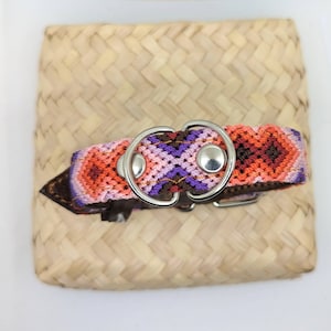 May include: A colourful dog collar with a geometric pattern in shades of orange, pink, purple and brown. The collar has a silver metal D-ring.