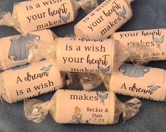Puede incluir: Una colección de pequeños favores envueltos con un tema de Cenicienta en azul y blanco. Cada favor tiene un pájaro azul y el texto "Un sueño es un deseo que tu corazón hace". Un favor tiene el texto "Beckie & Dan 7.7.23".