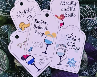 Puede incluir: Cinco etiquetas de regalo blancas con diferentes diseños de temática Disney. Cada etiqueta presenta una copa de vino con un personaje diferente de una película de Disney. Las etiquetas incluyen el texto "Drinker", "Bibbidi Bobbidi Booze", "Beauty and the Bottle", "Let it Flow", y "Laura's Hen do!"
