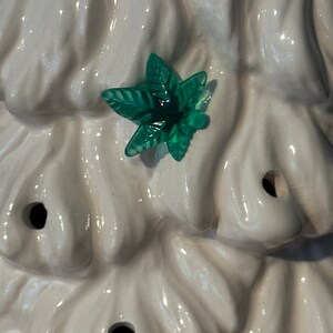 May include: White ceramic Christmas tree with a green glass leaf ornament.