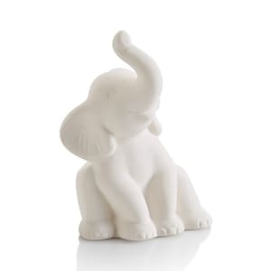 May include: White ceramic elephant figurine with a raised trunk and a playful expression. The elephant is sitting with its legs tucked under its body.
