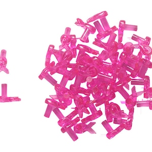 Può includere: Un grande mucchio di ciondoli a nastro di plastica rosa. I ciondoli hanno la forma di un nastro con un anello nella parte superiore. I ciondoli sono tutti a fuoco e sono disposti in uno schema casuale.