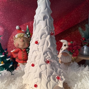 May include: White ceramic Christmas tree with holly leaf design and red berry accents. The tree is on a white base.