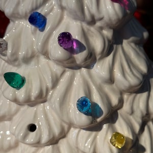 May include: White ceramic Christmas tree with colorful light bulbs. The bulbs are red, blue, green, purple, and yellow.