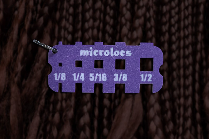 Pu&ograve; includere: Misuratore in plastica viola con un anello di metallo per misurare diverse dimensioni di filato. Il misuratore ha il testo "microlocs" e le seguenti misure: 1/8, 1/4, 5/16, 3/8, 1/2.