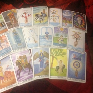 Puede incluir: Un despliegue de cartas de tarot sobre una superficie de tela roja. Las cartas están dispuestas en filas y presentan ilustraciones coloridas de varios símbolos y figuras. Las cartas incluyen la Reina de Pentáculos, La Suma Sacerdotisa, el As de Bastos, El Carro, La Estrella, La Rueda de la Fortuna, El Rey de Copas, La Sacerdotisa de la Luna, el As de Copas, El Mundo, el As de Espadas, La Templanza, El Loco, La Rueda de la Fortuna, La Fuerza, El Rey de Espadas.