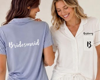 May include: Two pajama sets consisting of short-sleeved button-down shirts and shorts. One set is light blue with the word Bridesmaid on the back. The other is white with a pocket featuring the name Brittany and the initial B. Text includes SWEET NOVEMBER.