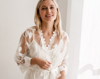 May include: White lace robe with floral embroidery and a tie sash. The robe is sheer and has a delicate, feminine look.