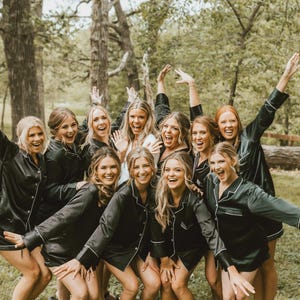 May include: A group of individuals wearing matching black button-down pajama shirts with white piping trim. The shirts feature long sleeves, a collared neckline, and a front button closure. The text McKenna Christine Photography is visible at the bottom.