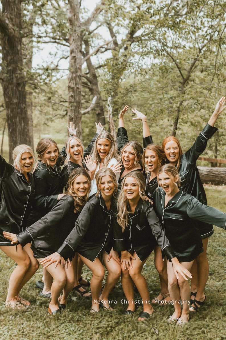 May include: A group of individuals wearing matching black button-down pajama shirts with white piping trim. The shirts feature long sleeves, a collared neckline, and a front button closure. The text McKenna Christine Photography is visible at the bottom.