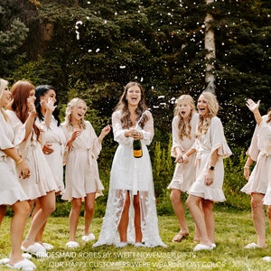 May include: A group of women wearing white and cream-colored robes are celebrating with champagne. They are standing in a grassy area with trees in the background. The text "BRIDESMAID ROBES BY SWEET NOVEMBER GIFTS OUR HAPPY CUSTOMERS WERE WEARING OAT COLOR" is visible at the bottom of the image.