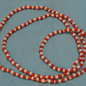 May include: A long strand of red and white beads, strung together in a repeating pattern. The beads are small and round, and the strand is coiled into a circle.