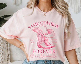 Puede incluir: Camiseta rosa con un gráfico rosa de botas de vaquero y un sombrero. El texto dice "Same Cowboy Est. 2024 Austin, Texas Forever Olivia's Bachelorette".