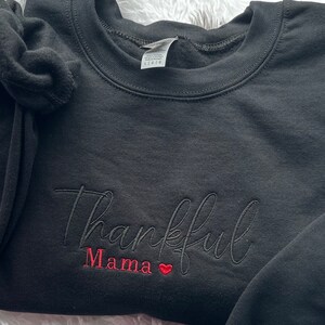 May include: Black sweatshirt with the text "Thankful Mama" embroidered in black and red with a small red heart.