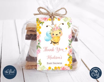 May include: A yellow and black bee with a pink flower crown holding a heart-shaped honey pot. The bee is surrounded by pink and white flowers and a honeycomb pattern. The text "Thank You Madison's Baby Shower" is printed on the tag.