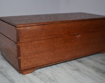 May include: A wooden box with a hinged lid and a rich brown finish. The box has a slightly rounded shape and sits on four small feet.