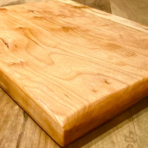 May include: A rectangular wooden chopping board made of cherry wood. The board has a natural wood finish and a smooth surface.