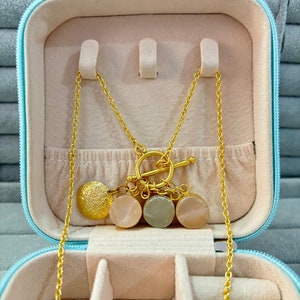 May include: A gold chain necklace with a toggle clasp and three round charms. The charms are pink, green, and white. The necklace is in a light blue jewelry box.