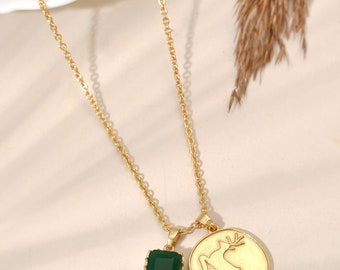 May include: A gold chain necklace with two pendants. One pendant is a green gemstone in a gold setting. The other pendant is a gold circle with a deer silhouette.