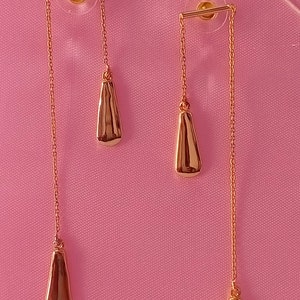 May include: A pair of gold dangle earrings with two teardrop-shaped charms on each earring.