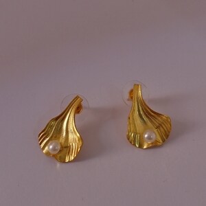 Peut inclure: Une paire de boucles d'oreilles dorées avec un accent de perle. Chaque boucle d'oreille présente un design texturé en forme de feuille.