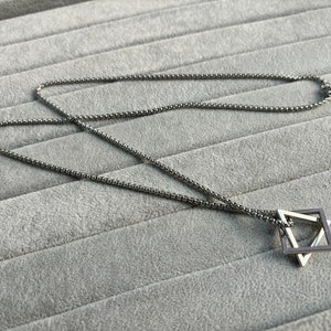 May include: A silver chain necklace with a geometric pendant. The pendant is made of two overlapping squares.