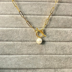 May include: A gold chain necklace with a toggle clasp and a single white pearl pendant.
