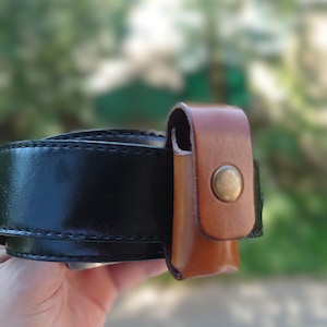 Könnte beinhalten: Ein brauner Ledergürtel mit einer braunen Ledertasche, die daran befestigt ist. Die Tasche hat einen Metallknopfverschluss.