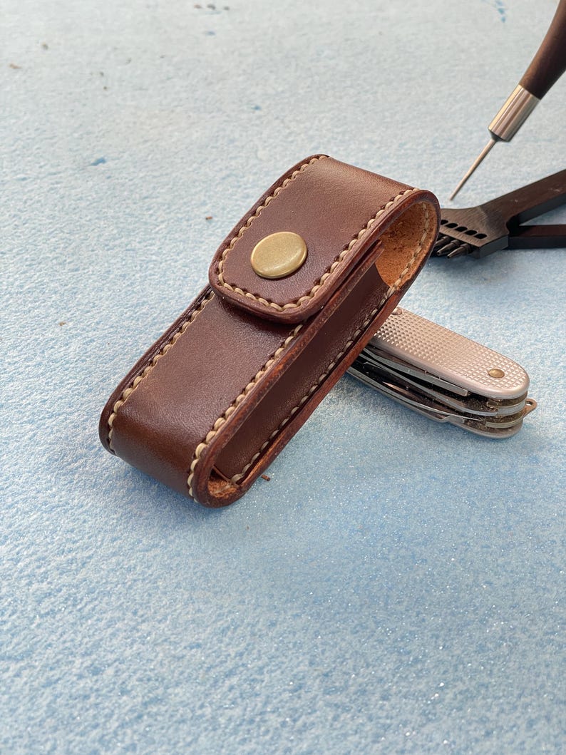 May include: A white ceramic mug with a black handle and the text "But First, Coffee" in a bold, black font. The mug is set against a blurred background, suggesting a cozy setting.