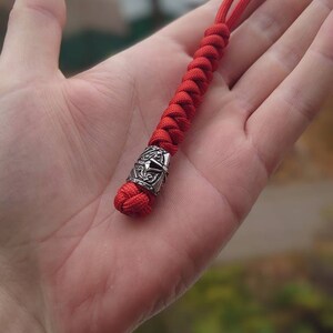 May include: A red paracord keychain with a silver metal bead featuring a decorative design.