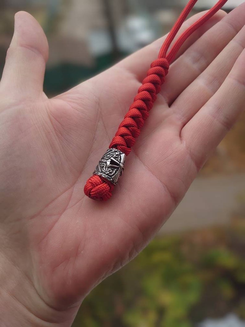 May include: A red paracord keychain with a silver metal bead featuring a decorative design.