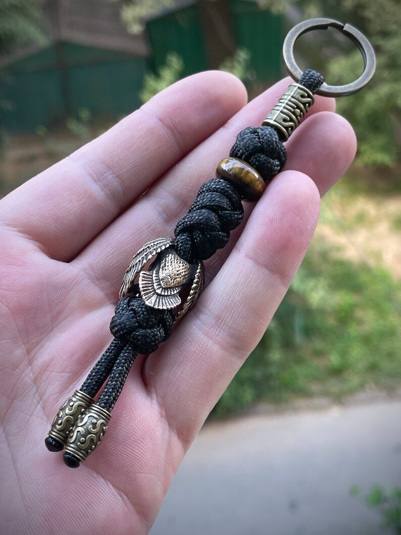 May include: Black paracord keychain with a brass owl charm, a tiger's eye bead, and a brass bead with intricate designs.