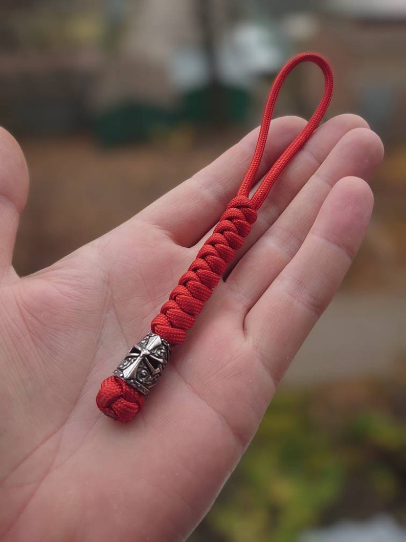 May include: A red paracord keychain with a silver knight helmet bead.