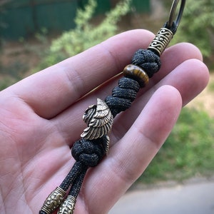May include: Black paracord keychain with a brass eagle charm, a tiger's eye bead, and a brass key ring.