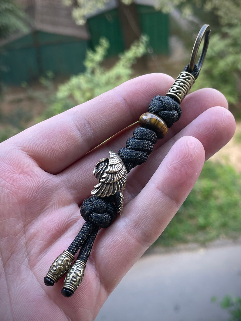 May include: Black paracord keychain with a brass eagle charm, a tiger's eye bead, and a brass key ring.