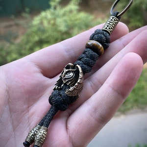 May include: A black paracord keychain with a brass owl charm, a tiger's eye bead, and a brass key ring.